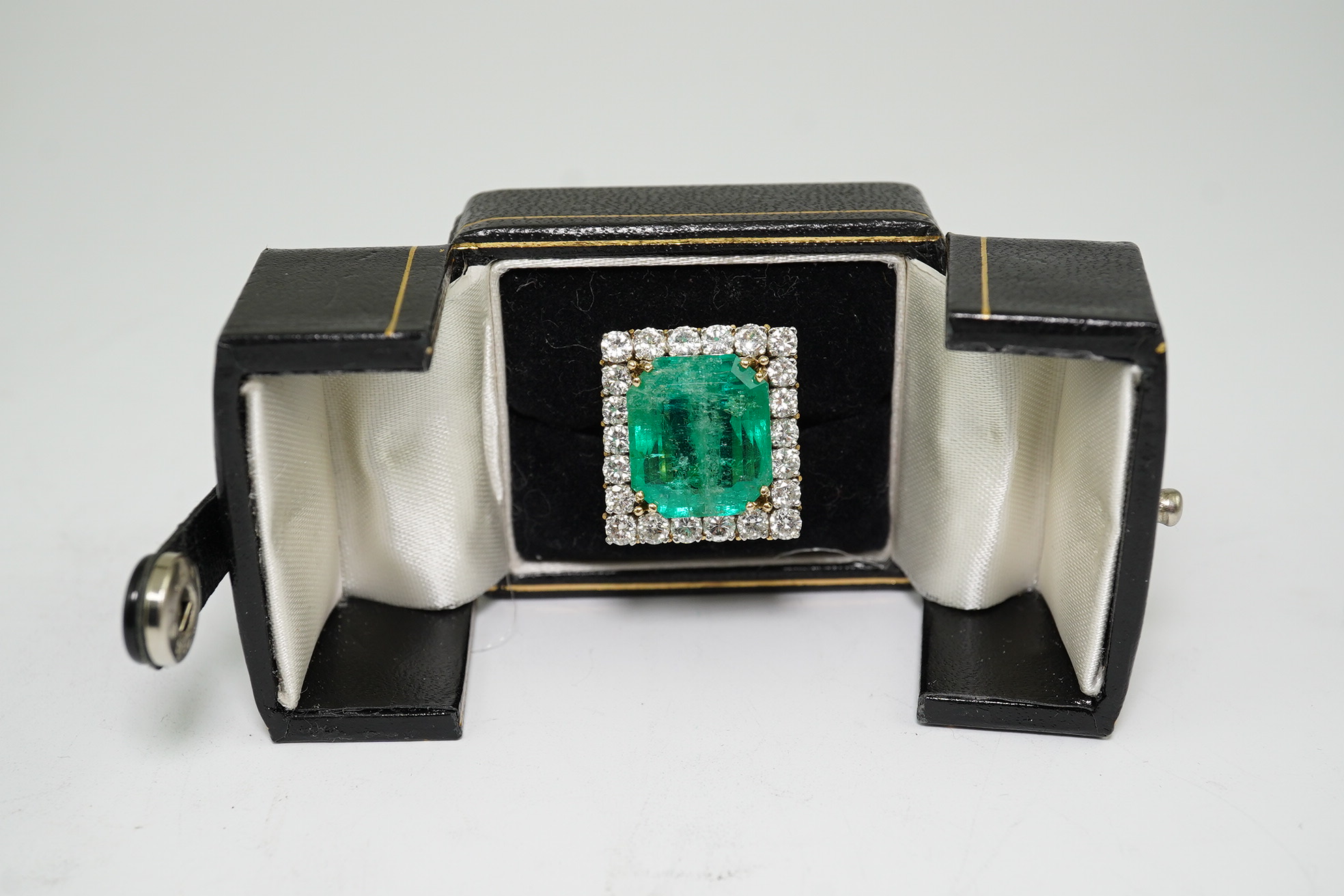 A Stern 18ct white and yellow gold, emerald and diamond dress ring, the central green emerald cut emerald approximately 8.0ct and surrounded by twenty two circular cut diamonds, approximately 2.7ct total